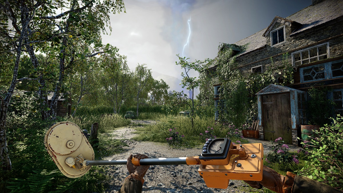 Atomfall: a hand holds some kind of metal detector, as the player stands in front of an old house with an overgrown front yard.